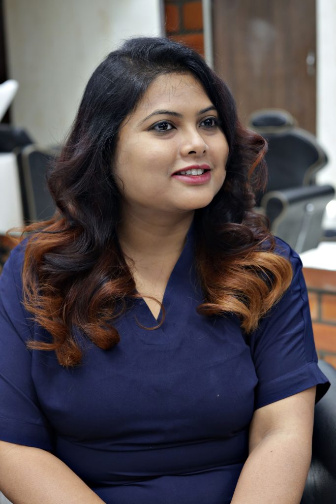 Portrait of a smiling woman with long, curly hair sitting in a salon chair.