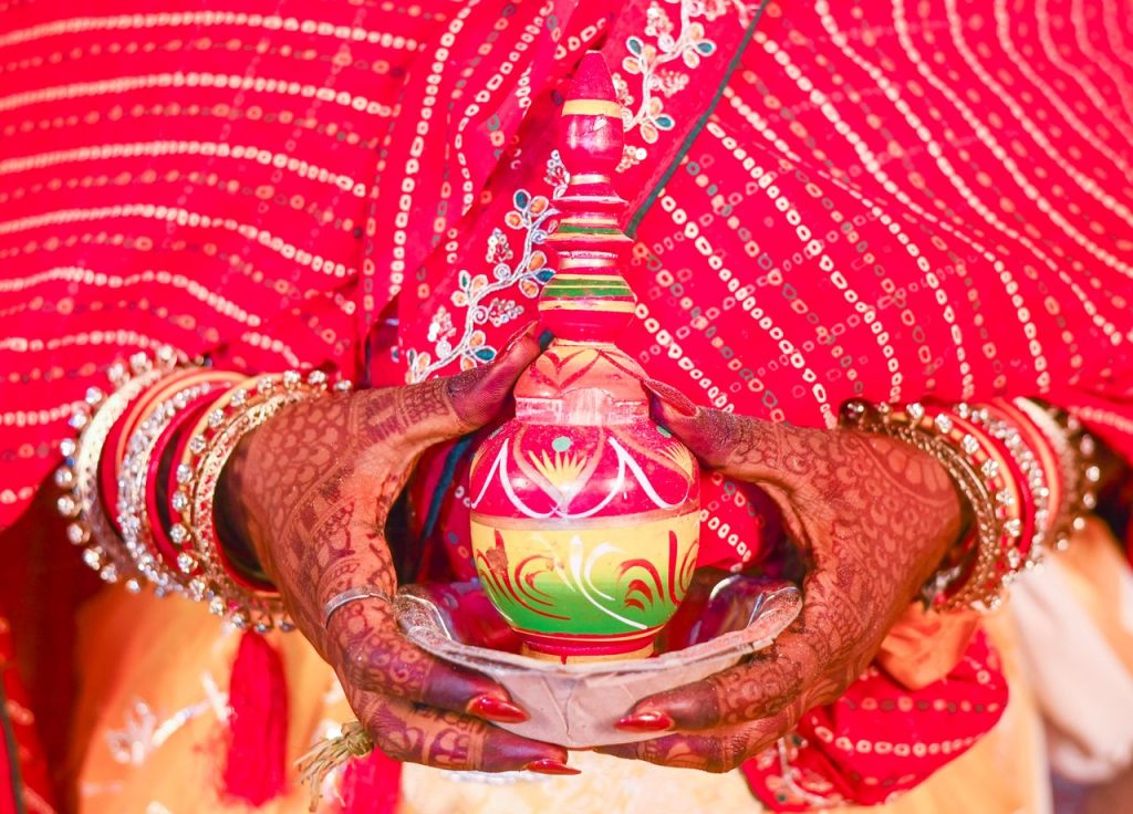 Close-up of a woman's hands with henna holding a decorative pot in a traditional Indian ceremony.